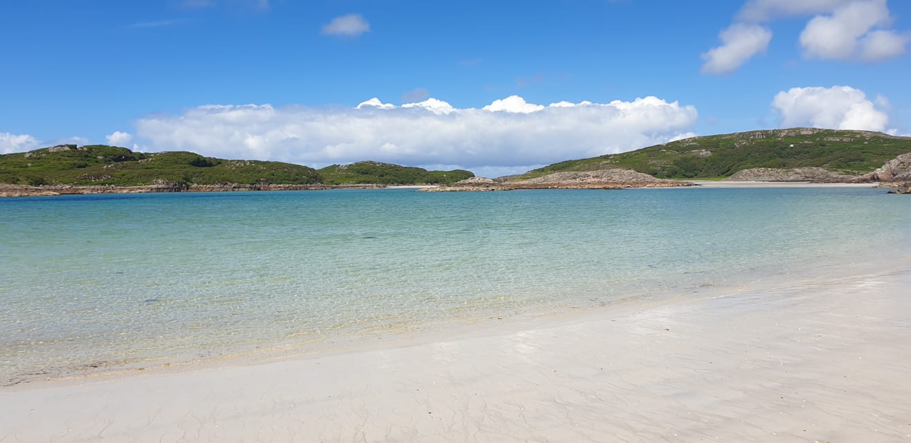 White sand beach at Knockvologan with gentle waves, turquoise sea, distant hills and blue skies