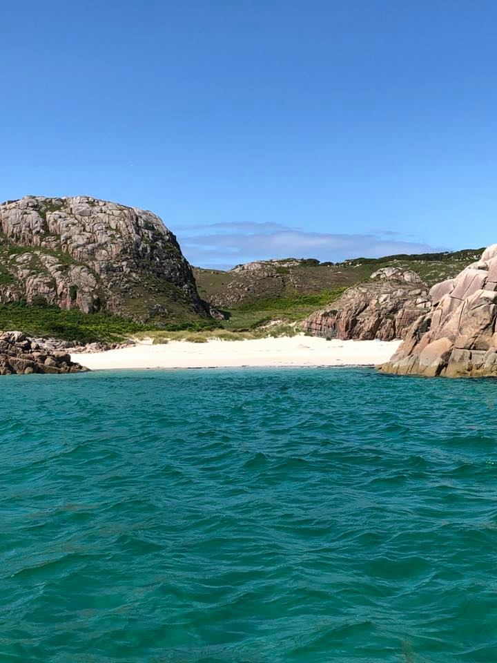 Turquoise sea and a white sandy cove, surrounded by tall pink granite rocks and blue sky