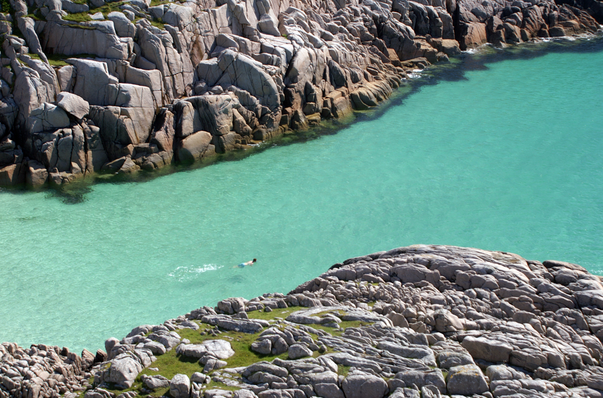 Swimmer exploring the bay between two rocky headlands in turquoise clear seas