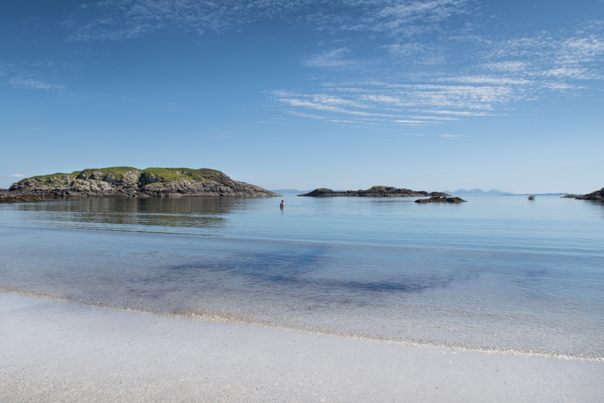 Wild swimmers enjoying the calm sea and turquoise blue skies on Uisken beach in Mull
