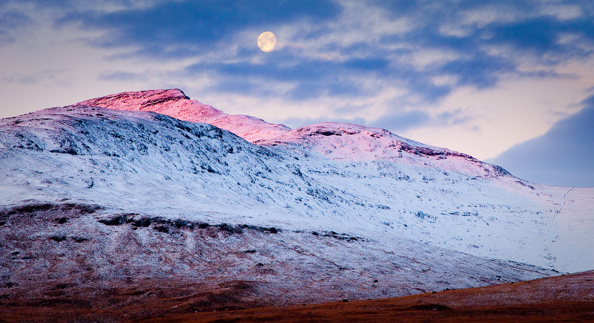 Winter on the Isle of Mull with snow-covered mountains, blue skies and the moon above