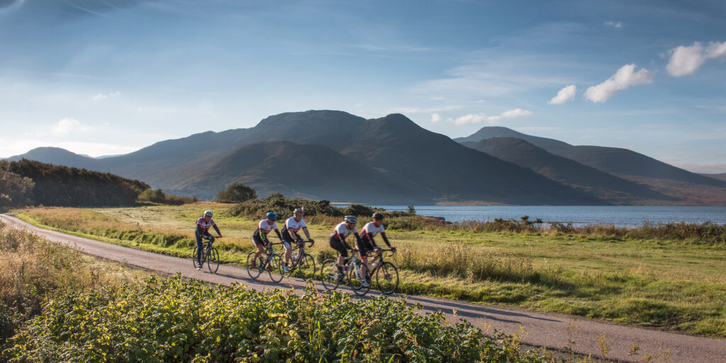 Group of cyclists along coast with mountains beyond