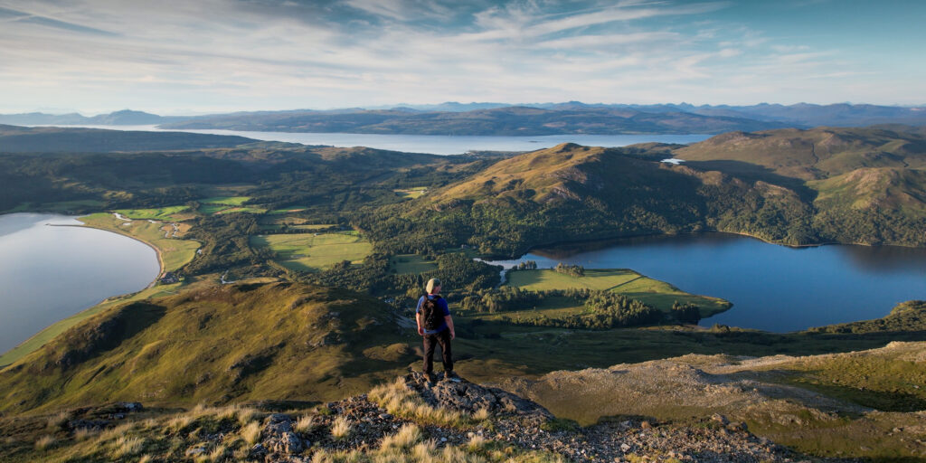 Walker standing on a hill looking to the sea and loch.