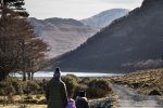 A family walk along the Loch Ba track with snowy mountains in the distance
