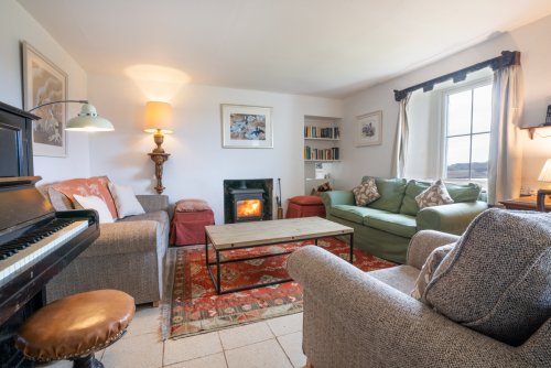 Living room at Tigh na Caora with wood stove, piano, books and games